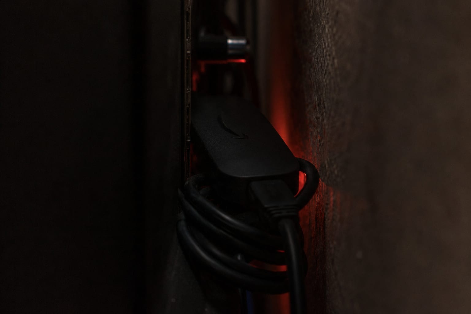 Streaming stick wedged in the tight gap behind a wall-mounted television with a warm glow suggesting heat